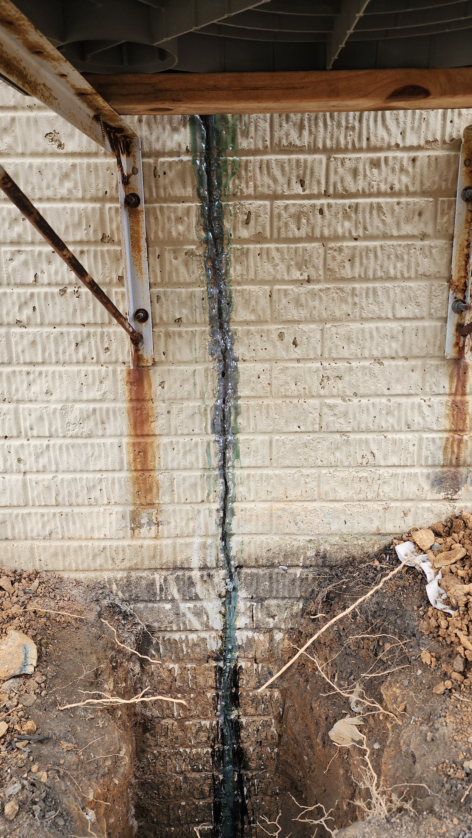 Vertical crack in block foundation repaired with epoxy, showing rust stains