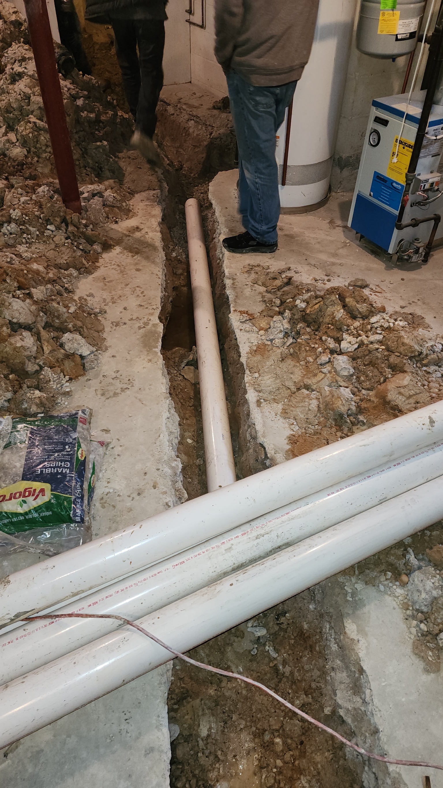 Workers installing drainage pipe in excavated basement trench